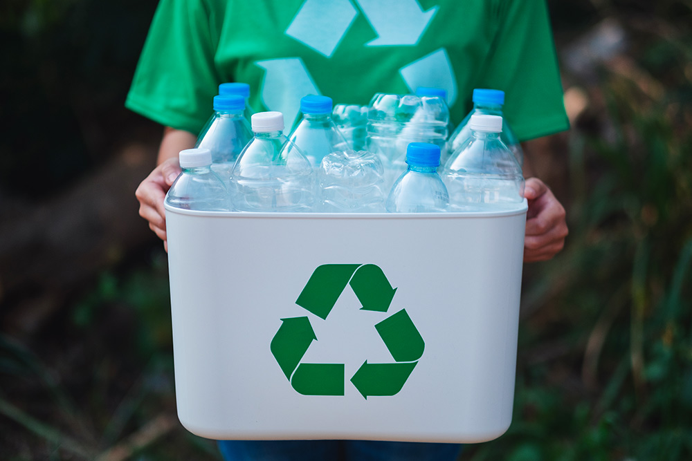 une personne tient un bac avec un signe “recyclage” rempli de bouteilles plastiques